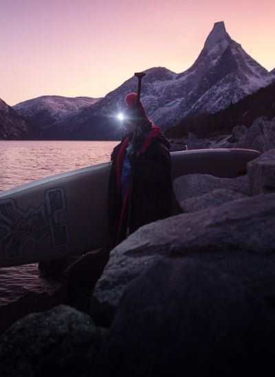 Person carrying stand up paddle board in front of mountains