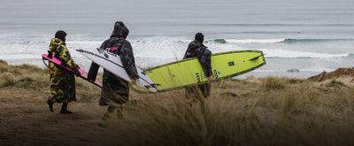 dryrobe® Ambassadors, The Skinners, carrying surfboards in front of a beach