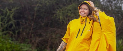 Woman stood in front of trees smiling, wearing dryrobe® Waterproof Poncho with hood up