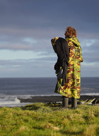 Man stood facing the sea holding a wetsuit