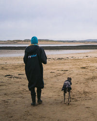 Woman walking away from camera on a beach with her dog, wearing Black Blue dryrobe® Advance Short Sleeve