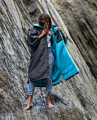 Woman stood on top of rocks on a beach, wearing Black Blue dryrobe® Advance Short Sleeve
