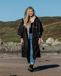 Woman walking towards camera on beach, wearing Black Grey dryrobe® Advance Short Sleeve