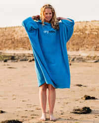Woman stood on a sunny beach, wearing  Cobalt Blue Organic Towel dryrobe®
