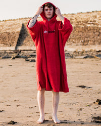 Man stood on a beach, wearing Red Organic Towel dryrobe® with hood up
