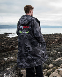 Man stood with back to the camera on a beach, wearing OCR dryrobe® Advance Limited Edition