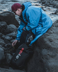 Man sat on rocks on the beach next to dryrobe® Compression Travel Bag