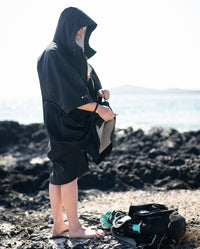Woman stood on a beach, zipping up dryrobe® Lite