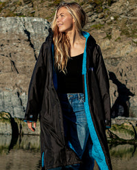 Woman stood on beach, wearing unzipped Black Blue dryrobe® Advance Long Sleeve