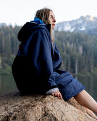 Woman sat by a lake on a rock, wearing  Navy Grey dryrobe® Advance Long Sleeve