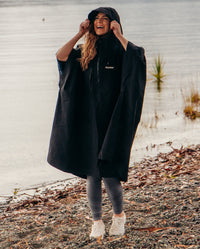 Woman stood in front of lake laughing, pulling hood up on Black dryrobe® Waterproof Poncho