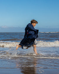 Boy running through shoreline wearing Navy Grey dryrobe® Advance Kids Long Sleeve