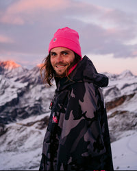 *MALE* stood in mountains wearing Black Camo Pink dryrobe® Advance and Pink dryrobe® Eco beanie
