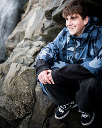 *MALE* crouched on a rock smiling, wearing  Blue Camo dryrobe® Waterproof Poncho 