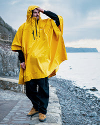 *MALE* stood on wall on the beach wearing Yellow dryrobe® Waterproof Poncho
