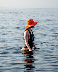1|Woman stood at waist depth in the sea and sun, wearing Orange dryrobe® Quick Dry brimmed hat