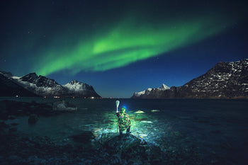 Cal Major, standing on the shoreline preparing to SUP under the Northern Lights in Norway