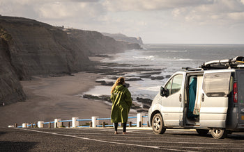 Cal Major stood in green dryrobe® by her van next to a beach in Europe 
