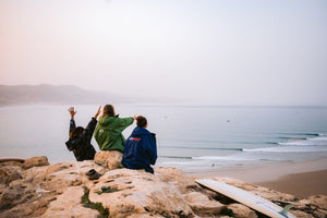 Three people sat on a rock looking at the beach in dryrobes 