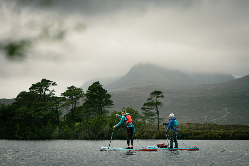 Two people SUPing on a lake with a misty hill in the background