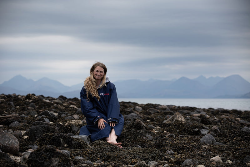 Cal Major sat on rocks by the ocean wearing a navy dryrobe® Advance change robe