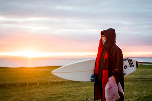 Hottest UK Surf Spots blog hero image featuring a surfer hold a board and wearing a dryrobe Advance 