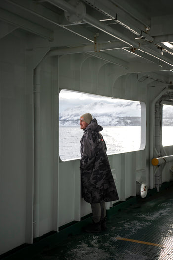 A man in a dryrobe looking out to a snowy landscape from a boat window 