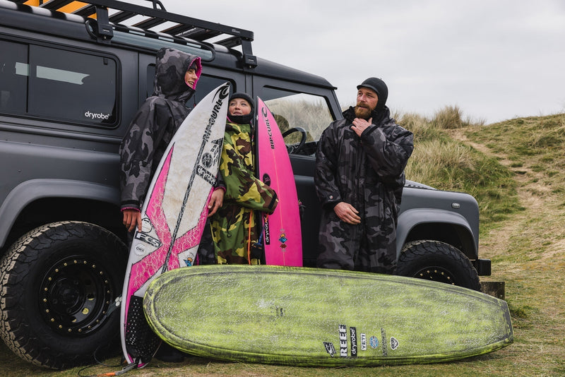 A family in wetsuits and dryrobes stood outside a car ready to go for a surf 