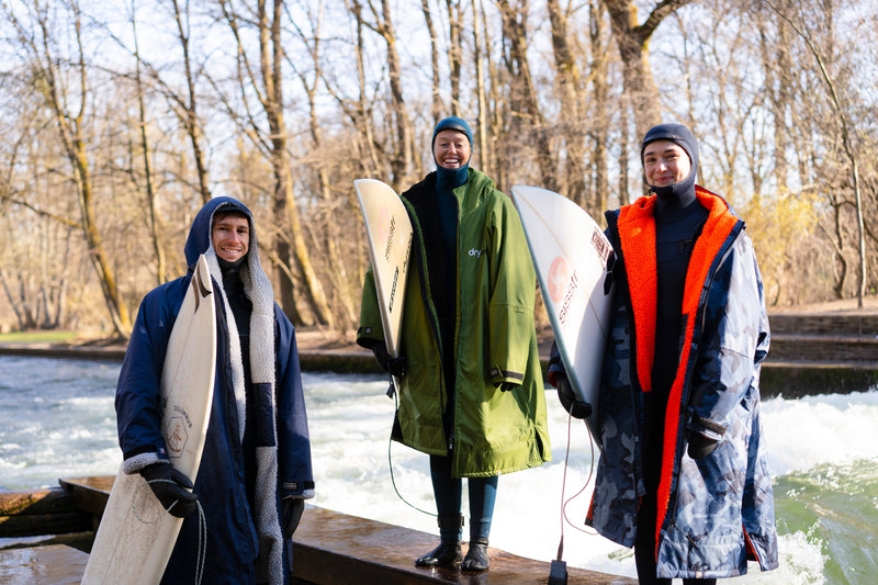 German surfers Camilla Kemp, Maya Sauer and Finn Springborn at the Eisbach River wearing wetsuits and Dryrobes 
