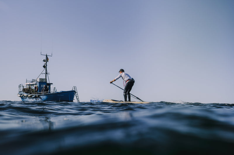 A man SUPing with a boat in the background on a Fehmarnbelt Crossing