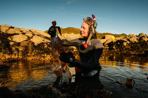 A person in a snorkel holding kelp in a rock pool 