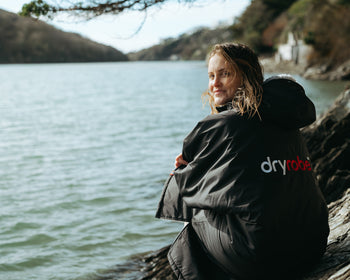 Sophie Hellyer sat in a dryrobe by the water and looking at the camera 