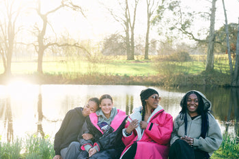 4 Black women behind the scenes of Swim Sistas smiling on a bench with a lake behind them