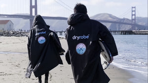 Two surfers walking toward the Golden Gate Bridge wearing black Dryrobe Advance change robes featuring the City Surf Project patch.
