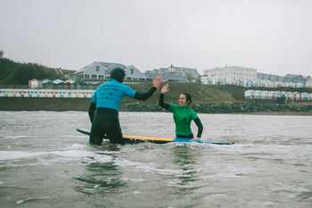 An instructor and surfer high-fiving in the sea while surfing at Bude Beach