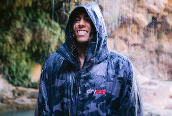 A man wearing a dryrobe under a waterfall 