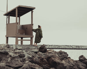 Lexie Kelly stood on the shore holding onto a building whilst wearing a green dryrobe changing robe