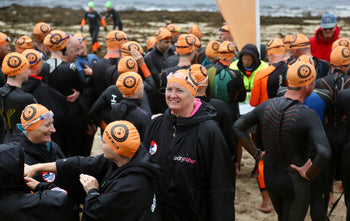 Swimmers stood on the beach wearing orange swim caps at the Scilly Swim Challenge 2022