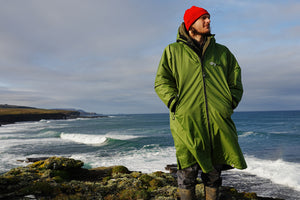 Man standing on shoreline wearing Forest Green dryrobe® Advance changing robe made with recycled fabrics.