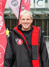 Person wearing a dryrobe with a 'Red Nose Day' logo, standing in front of promotional banners.