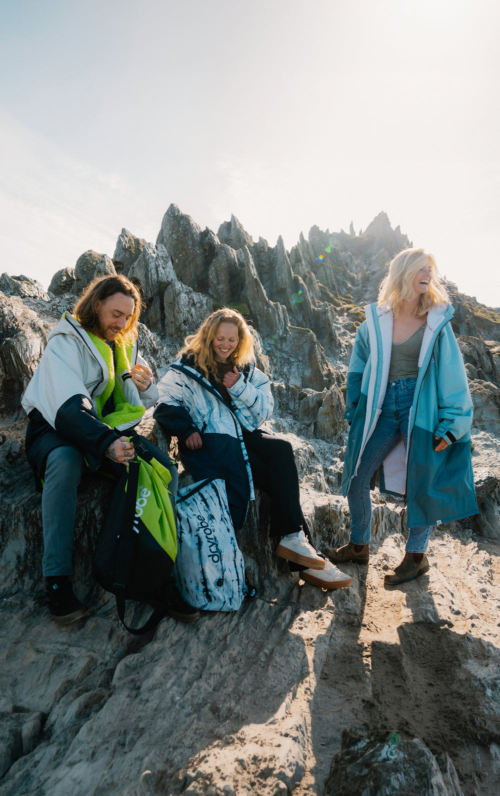 Three women sitting on a rocky outcrop with scenic mountains in the background