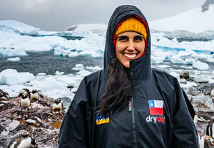 Person wearing a black Dryrobe® change robe with a Chilean flag on it, standing in front of icebergs and penguins.