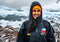 Person wearing a black Dryrobe® change robe with a Chilean flag on it, standing in front of icebergs and penguins.