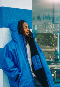 Man wearing a blue wearing a Dryrobe® changing robe standing against a blue and white wall with a glass door in the background.