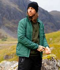 Man wearing a green Dryrobe® jacket and black beanie standing in a mountainous landscape