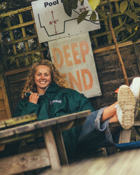 Female sitting on wooden bench wearing AW25 Green Dryrobe® advance long sleeve 
