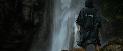 Person wearing a black Dryrobe Lite standing in front of a waterfall.