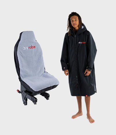 A person wearing a black dryrobe stands beside a black and light grey car seat cover with the dryrobe logo, on a light grey studio background.