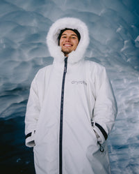 Man stood in ice cave, wearing dryrobe Advance Long Sleeve Alpine Range change robe in Alpine White with hood up
