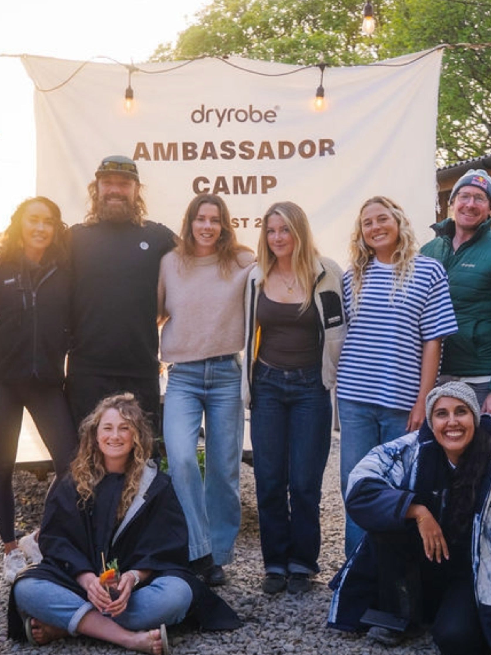 Group of people posing with a banner at an outdoor event, with wooden structures in the background.